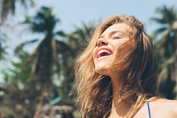 A woman smiles with her eyes closed as the sun rays shine down upon her face.