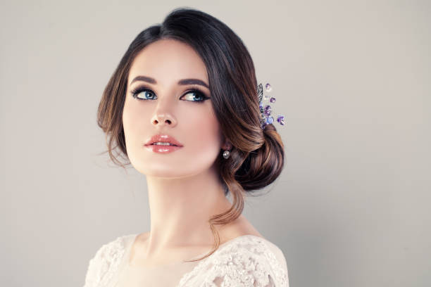 A bride wearing a lace wedding dress and her hair in a loose bun looks toward the upper righthand corner of the picture.