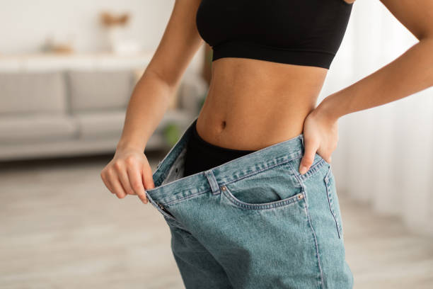 A woman pulling her oversized jeans away from her body at the waistband